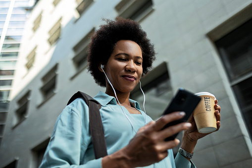 Young African-American woman on a coffee break looking at smart phone wearing headphones