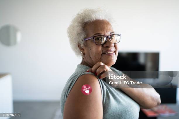 Portrait Of A Senior Woman Showing Arm With Got Vaccinated Sticker On Stock Photo - Download Image Now