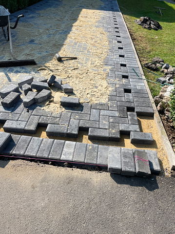 Stock photo showing an elevated view of a herringbone patterned driveway being constructed with grey, rectangular blocks, with brick edging where the drive meets the tarmac pavement.