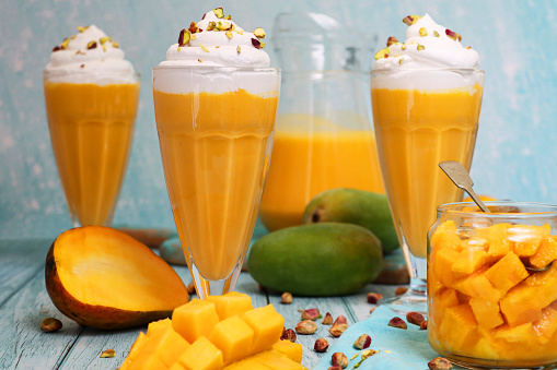 Stock photo showing mango smoothies / milkshake drinks, served in American diner-style knickerbocker glasses. These drinks have been made with pureed mango, milk and whipped cream, and topped with chopped Pistachio nuts.