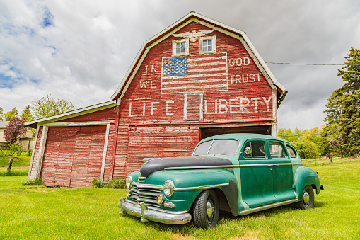 Latah, Washington, USA. May 24, 2021. Vintage Plymouth Super De Luxe automobile and a weathered red a barn.
