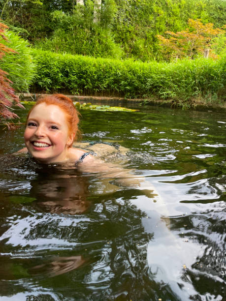 ろ過された水の中で大きな鯉の魚と一緒に泳ぐ魅力的な赤毛の女性、カエデ/サー、ランタン、竹、レンガの縁取りが池の水に覆われた美しい禅の日本庭園を持つ鯉の池のクローズアップ画像 - iris single flower flower outdoors ストックフォトと画像