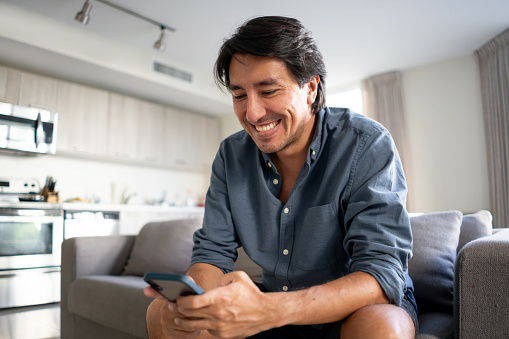 Latin American man at home texting on his cell phone and looking very happy - lifestyle concepts