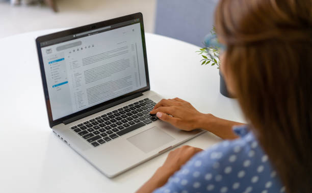 woman working at home and reading e-mails on her laptop - correspondência imagens e fotografias de stock