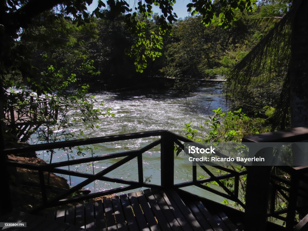 Paraiba do Sul river in the city of Guararema, with its waters covered by silvery reflections, framed by vegetation and a shaded wooden deck. Paraiba do Sul river in the city of Guararema, with its waters covered by silvery reflections, framed by vegetation and a shaded wooden deck - Guararema, SAO PAULO, BRAZIL. River Stock Photo