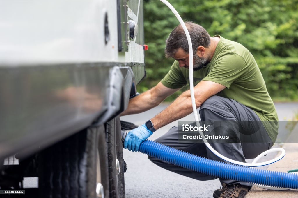 Man Emptying RV Sewer at Dump Station After Camping Camper Trailer Stock Photo