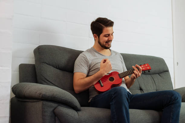 istock Latin man smiles while playing ukulele indoors. 1330817094