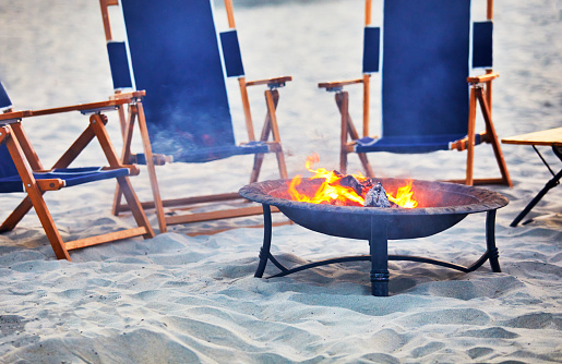 Fire pit on the beach with empty lounge chairs