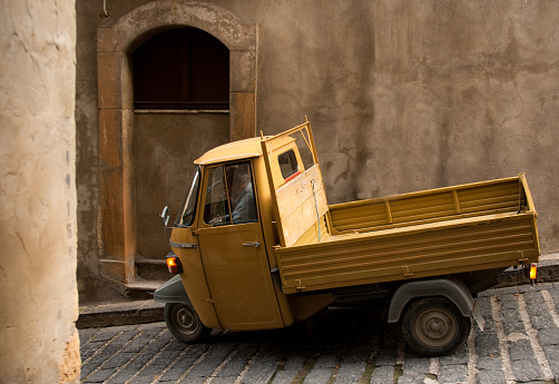 Piazza Armerina, Sicily, Italy: A vintage three-wheeled Piaggio Ape truck passing on a cobbled street in downtown Piazza Armerina.