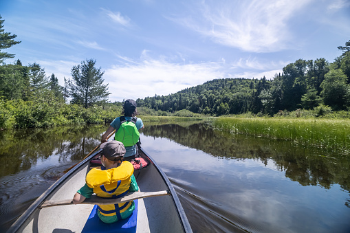 POV Family canoeing on Wapizagonke lake in Parc National de la Mauricie, Quebec, Canada in Summer. The mother and her son are rowing in directions to Chutes Waber Waterfalls.