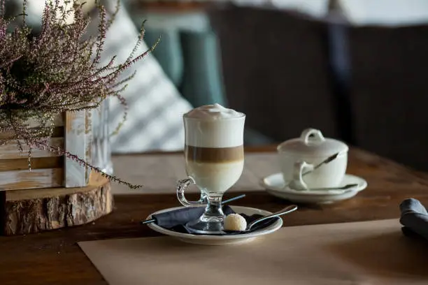 Hot latte macchiato coffee with tasty foam clear glass on dark wooden table serving with cinnamon and cane sugar.