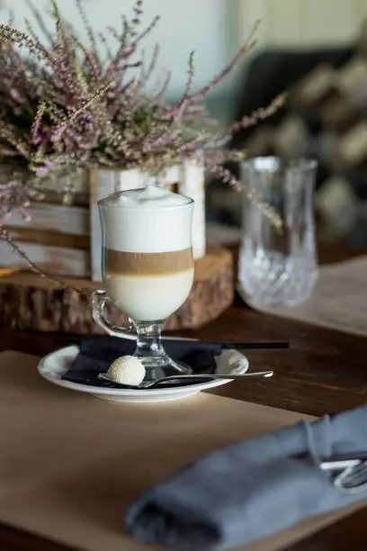 Hot latte macchiato coffee with tasty foam clear glass on dark wooden table serving with cinnamon and cane sugar.
