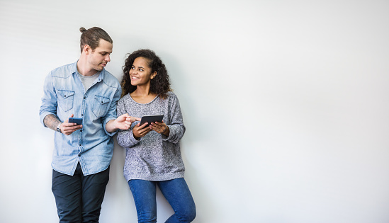 portrait of happy young couple using smartphone standing isolated over white wall background. Man and woman hands holding mobile phone, technology communication network online together concept