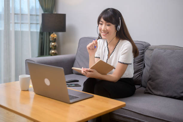 Beautiful young woman wearing headset is making video conference call via computer at home A beautiful young woman wearing headset is making video conference call via computer at home online tutors stock pictures, royalty-free photos & images