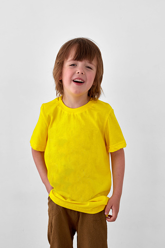 Glad young boy in yellow t shirt standing against white background and looking away