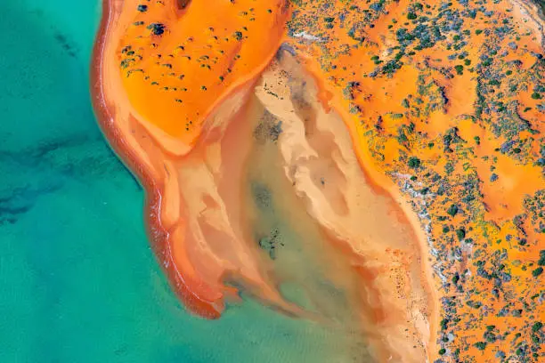 View of pristine blue-green water in shifting red deposition of sediment gradually moving through alluvial plains of locations surrounding Francois Peron National Park in Western Australia.