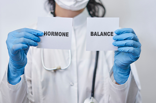 A female doctor holding two white cards with Hormone balance words. Hormone balance concept