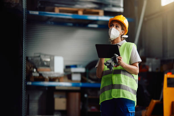 istock Female warehouse worker using touchpad while checking stock in storage room during COVID-19 pandemic. 1330843384