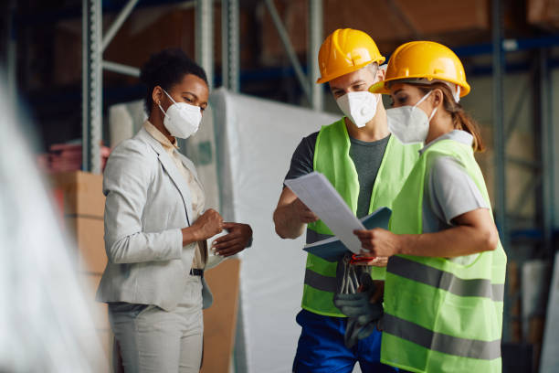 istock Warehouse workers going through delivery schedules with African American female manager during coronavirus pandemic. 1330843414