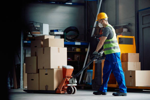 istock Full length of worker pushing pallet jack while working warehouse during coronavirus pandemic. 1330843432