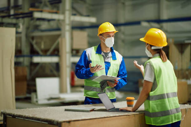 istock Warehouse worker discussing with female colleague while working in a storage room during coronavirus pandemic. 1330843458