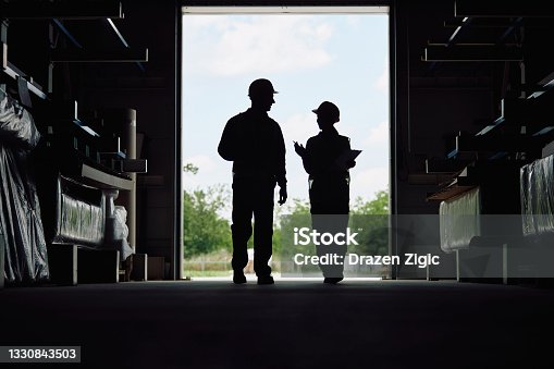istock Silhouette of warehouse workers talking at storage compartment. 1330843503