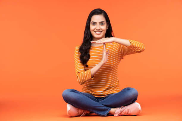 portrait of a young women showing time out signal sitting isolated over orange background Adult, young women backgrounds, India, Indian ethnicity, time out signal stock pictures, royalty-free photos & images