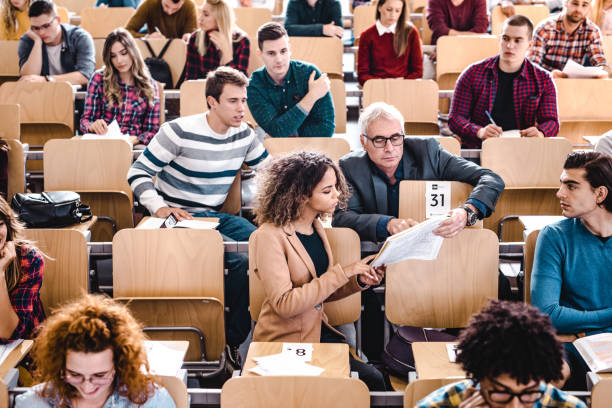 istock Senior teacher and his student reading a textbook at lecture hall. 1330844437