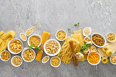 Pasta. Various kinds of uncooked pasta and noodles over stone background, top view with copy space for text. Italian food culinary concept. Collection of different raw pasta on cooking table