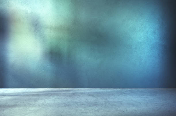 istock Teal textured wall and concrete floor in empty room for displaying your product, light coming through window, industrial atmosphere. 1330849256