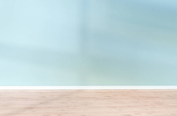 istock Light blue textured wall and wooden floor in empty room for displaying your product, light coming through window. 1330849284