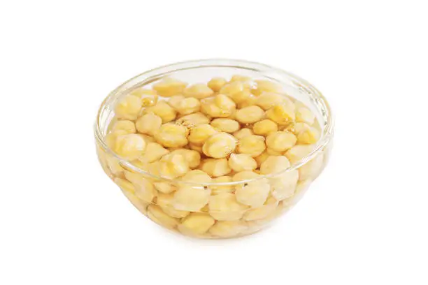 Cooking chickpeas. Soaking chickpeas in water. Glass bowl with soaked chickpeas on a white background.