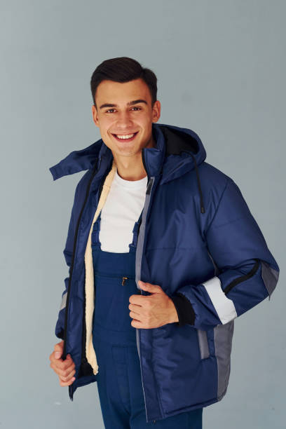 istock In warm jacket. Male worker in blue uniform standing inside of studio against white background 1330859096
