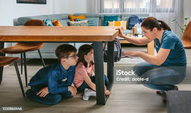 Mother Explaining To Her Children How To Protect Themselves In An Earthquake Stockfoto en meer beelden van Aardbeving