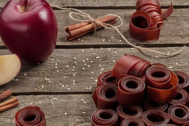 Photo of Rolls of fruit leather on wooden surface with apple and cinnamon
