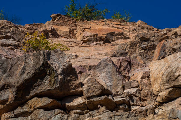 istock Granite rocks close-up on background blue sky with white clouds, green leaves on treetops. 1330862368