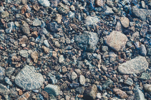 istock Smooth stones at bottom shallow mountain stream, rocky background close-up. Sun glare on smooth rocks at bottom stream 1330862388