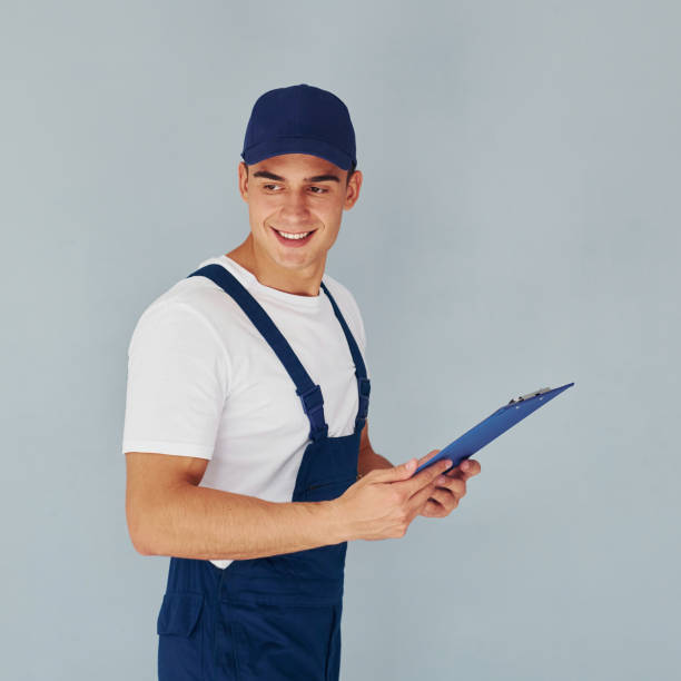 istock In cap and with notepad. Male worker in blue uniform standing inside of studio against white background 1330863785