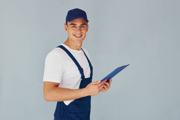 istock In cap and with notepad. Male worker in blue uniform standing inside of studio against white background 1330864374