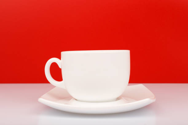 istock Close up of white ceramic coffee or tea cup on white table against red background 1330864804