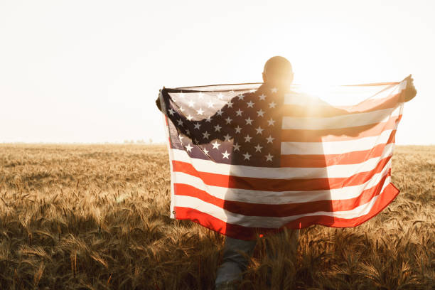 istock Young man holding American flag on back while standing in wheat field 1330866264