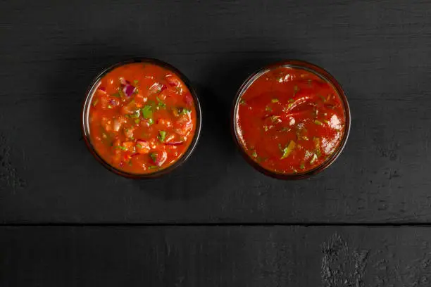 Photo of Tomato sauces in glass dipping bowls on black wooden background