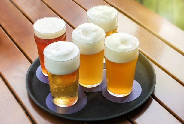 cinq bières froides avec des têtes mousseuses dans des verres sur un plateau - serving drink beer garden beer glass photos et images de collection