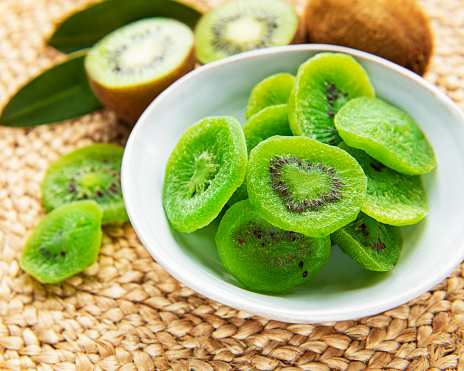 Pieces of dry kiwi in a bowl on a straw mat background