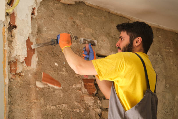 istock Young builder breaking up a house wall with a hammer and a chisel. 1330868876