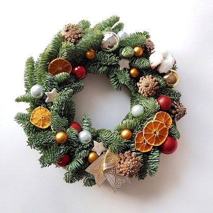 Christmas wreath on white wall. Cones, glass balls, dried mugs of oranges, Christmas stars, cotton bolls and fir tree branches.