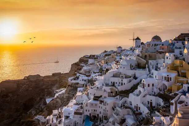 Orange summer sunset behind the beautiful village of Oia, situated at the edge of the cadera at Santorini island, Cyclades, Greece