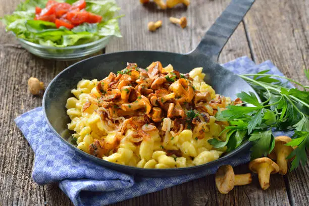 Vegetarian Swabian spaetzle with fried chanterelles and onions served in a frying pan