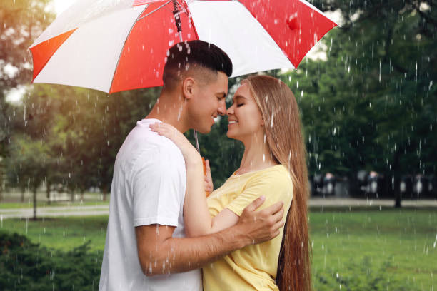 istock Lovely couple with umbrella walking under rain in park 1330873221