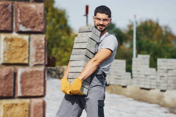 Holds bricks. Male worker in yellow colored uniform have job with pavement.